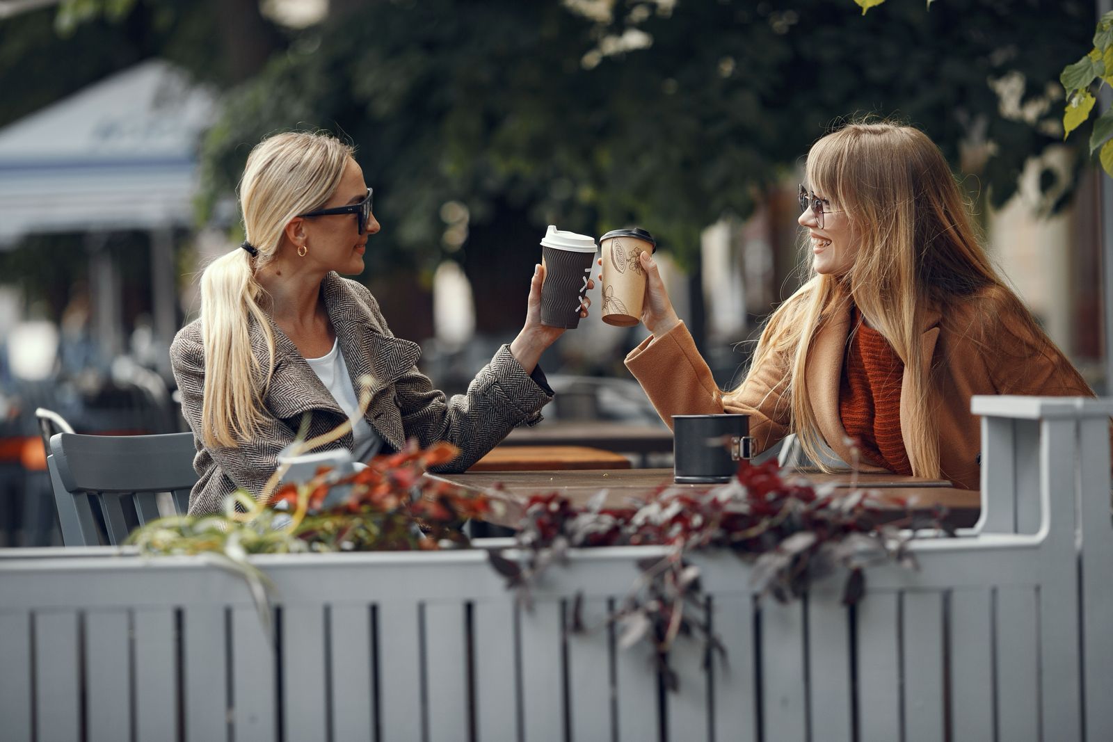 Deux amies attablées à la terrasse d'un café, qui trinquent avec leurs gobelets.